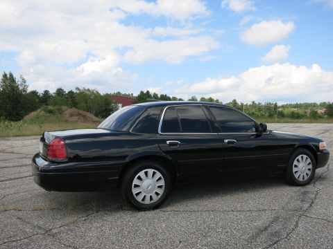 2001 Ford Crown Victoria - Side view of a black 2001 Ford Crown Victoria sedan parked on cracked asphalt under a cloudy sky.