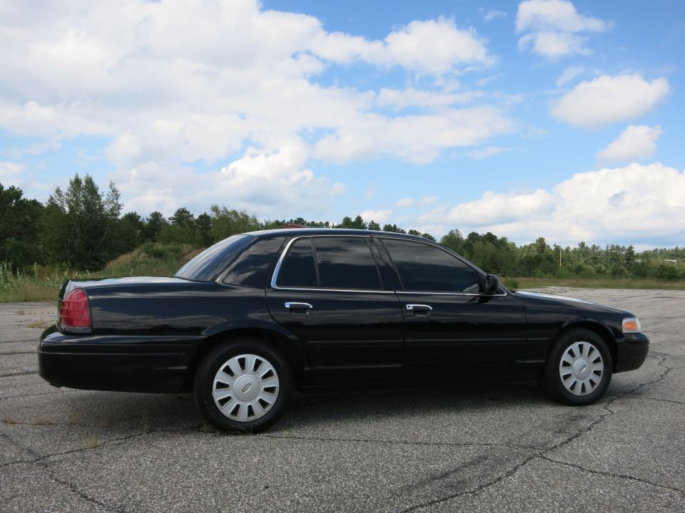 Side view of a black 2001 Ford Crown Victoria parked on asphalt with trees and clouds in the background