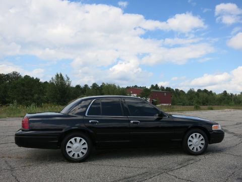 2001 Ford Crown Victoria - A black 2001 Ford Crown Victoria sedan is seen from the side under a cloudy sky.