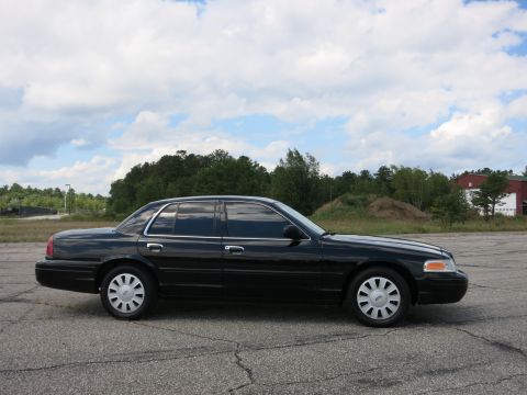 2001 Ford Crown Victoria - This black sedan is parked outdoors with trees and a building in the background under a cloudy sky.