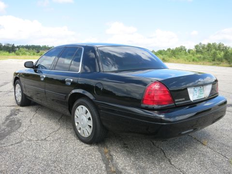 2001 Ford Crown Victoria - A black Ford Crown Victoria is parked on a cracked asphalt surface under a partly cloudy sky.