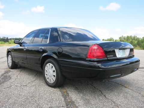 2001 Ford Crown Victoria - A black sedan is viewed from the rear quarter angle on a paved surface with trees in the background.