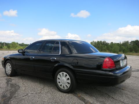 2001 Ford Crown Victoria - Rear quarter view of a black 2001 Ford Crown Victoria parked on asphalt under a cloudy blue sky.