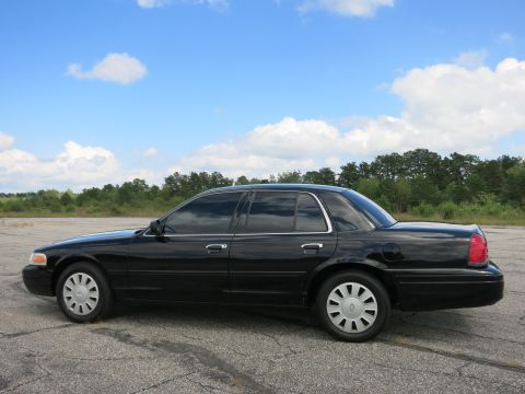 2001 Ford Crown Victoria - A black 2001 Ford Crown Victoria is parked on an asphalt lot under a partly cloudy sky.