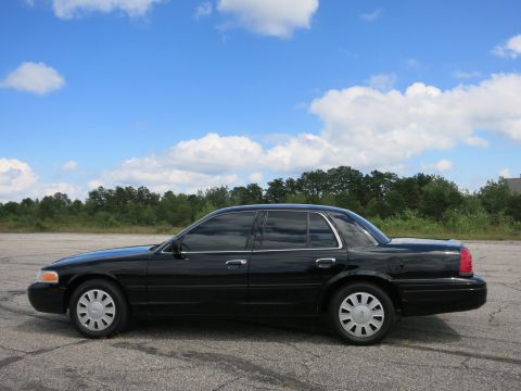 2001 Ford Crown Victoria - Side profile of a black 2001 Ford Crown Victoria sedan parked outdoors under a partly cloudy sky.