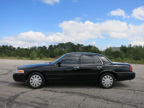 2001 Ford Crown Victoria - Side view of a black 2001 Ford Crown Victoria sedan under a partly cloudy sky.
