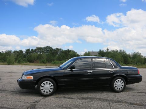 2001 Ford Crown Victoria - Side profile of a black 2001 Ford Crown Victoria sedan under a partly cloudy sky.