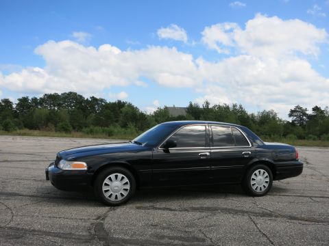 2001 Ford Crown Victoria - A black 2001 Ford Crown Victoria sedan is parked on an asphalt lot under a partly cloudy sky.
