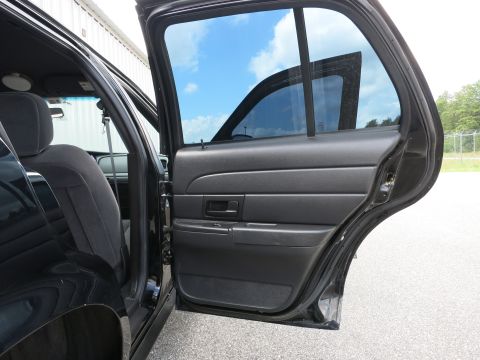2001 Ford Crown Victoria - View of the interior of a black car, focusing on the rear door panel and seat, with the door open to the outside.