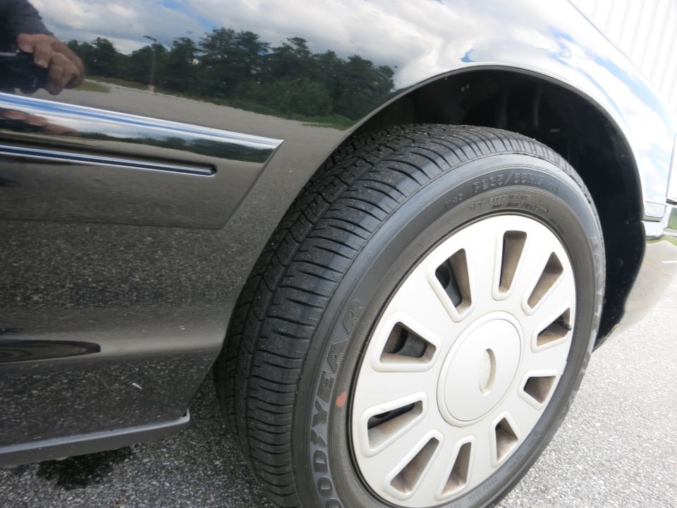 Close-up of a black car's front wheel and fender. The wheel has a silver hubcap with many spokes