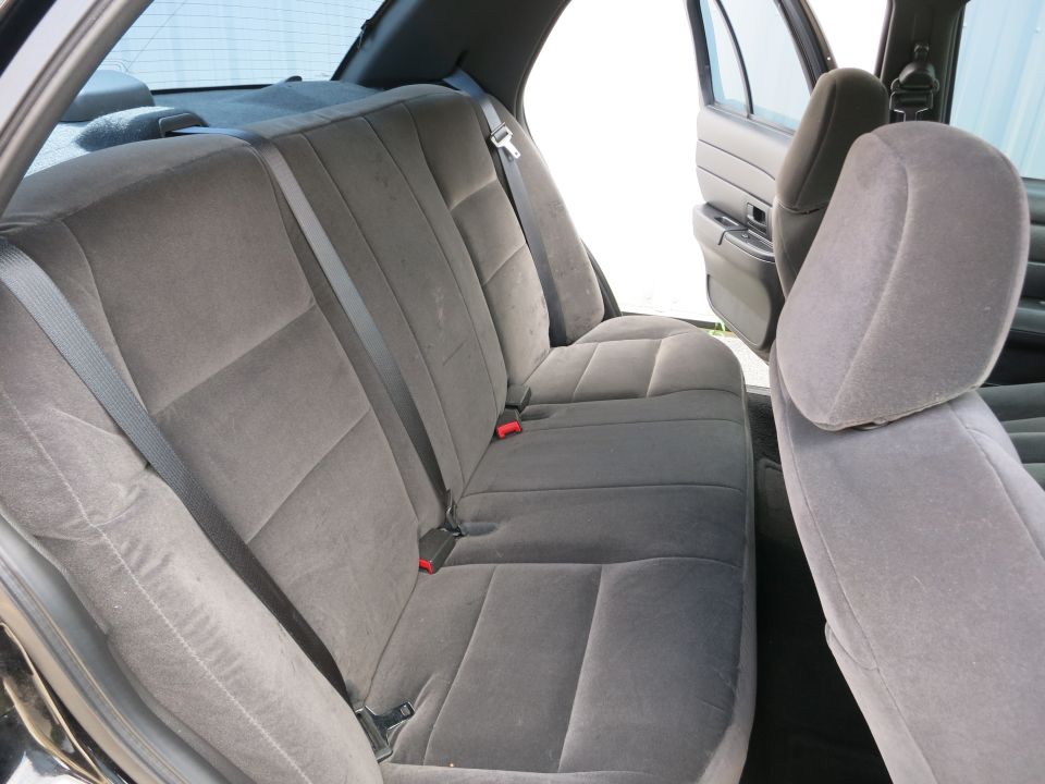 Back seat of a car with gray cloth upholstery and seatbelts. The rear doors are open