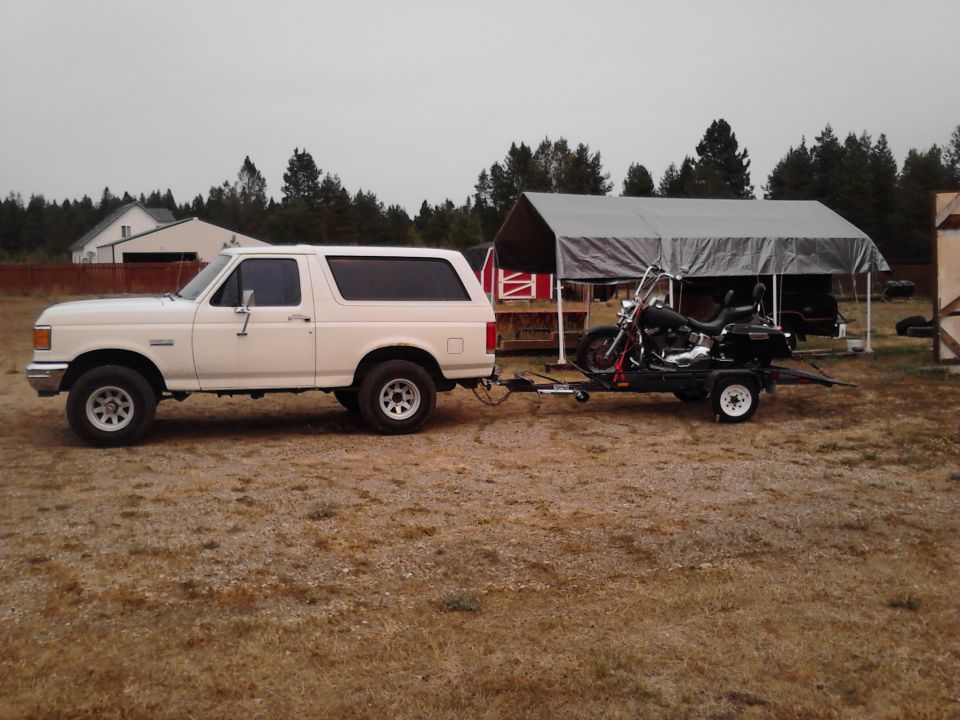 1990 Ford Bronco parked outside, towing a motorcycle on a small trailer