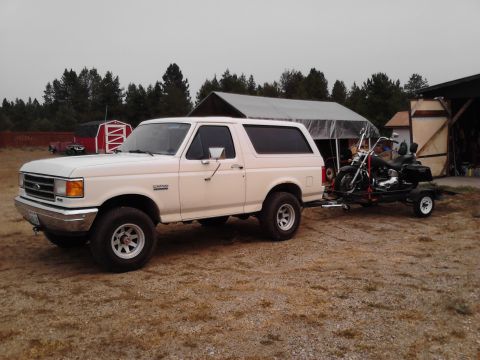1990 Ford Bronco - A white 1990 Ford Bronco is shown towing a motorcycle on a trailer in a rural setting.