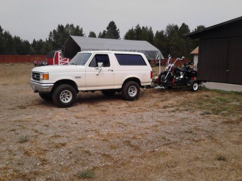 1990 Ford Bronco - A white 1990 Ford Bronco tows a motorcycle on a trailer in a rural setting.