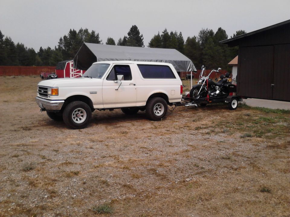 White 1990 Ford Bronco towing a motorcycle on a trailer