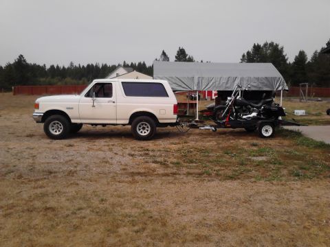 1990 Ford Bronco - A white 1990 Ford Bronco is seen from the side, towing a motorcycle on a trailer.