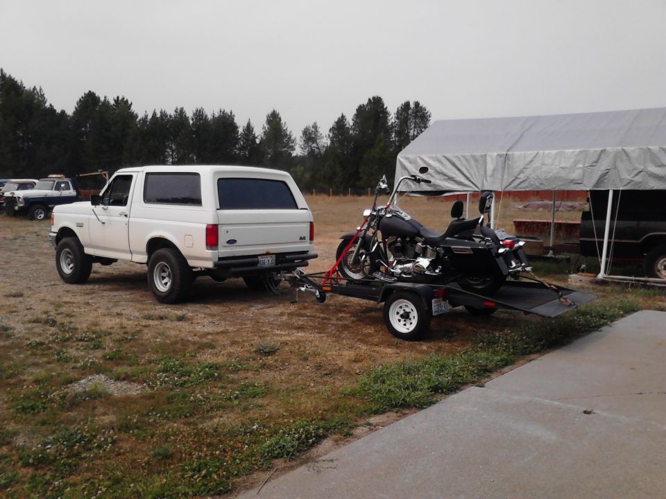 1990 Ford Bronco towing a Harley-Davidson motorcycle on a trailer, parked outdoors