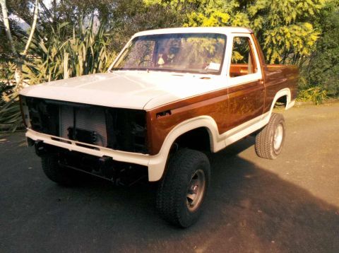 1982 Ford Bronco - A two-tone pickup truck with a lifted suspension and missing grille is parked outdoors.