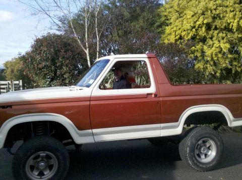 1982 Ford Bronco - Side view of a two-tone brown and white 1982 Ford Bronco with a driver visible.