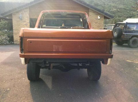 1982 Ford Bronco - The rear of an orange pickup truck is shown, with a second vehicle parked nearby.