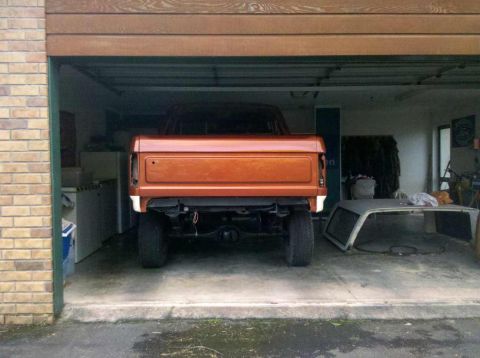 1982 Ford Bronco - Rear view of an orange 1982 Ford Bronco parked inside a garage, with its removable top nearby.