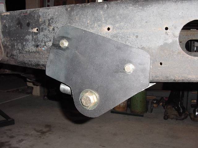 Black steel bracket with hex bolts mounted to rusty frame rail on 1987 Ford Bronco in garage