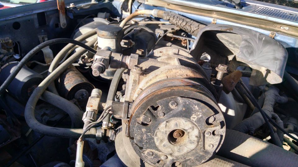Engine bay with AC compressor, hoses, and belts visible