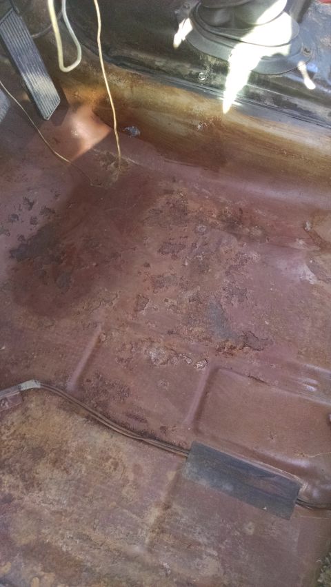 1979 Ford F-150 - The floor pan of a vehicle shows significant rust damage, with pedals visible in the upper left.