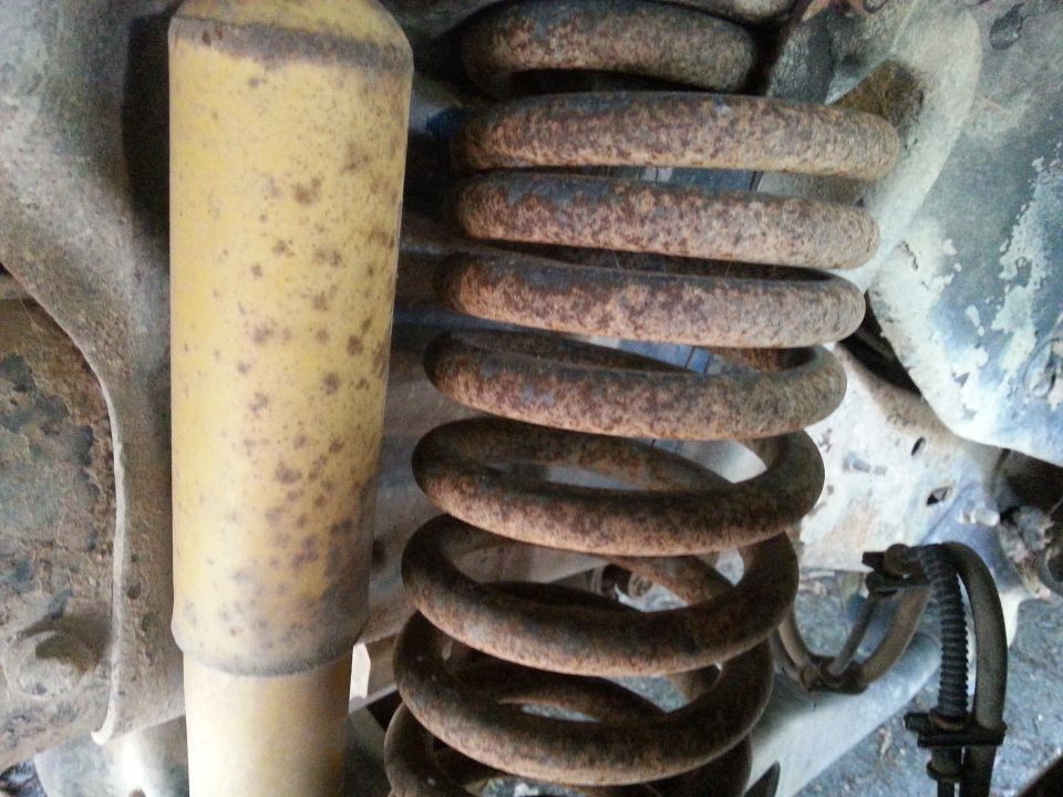 Yellow shock absorber next to a rusty coil spring, likely from a vehicle's suspension