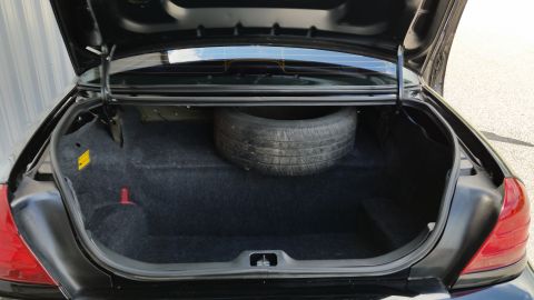 2001 Ford Crown Victoria - The open trunk of a car reveals a spare tire and dark carpeting.