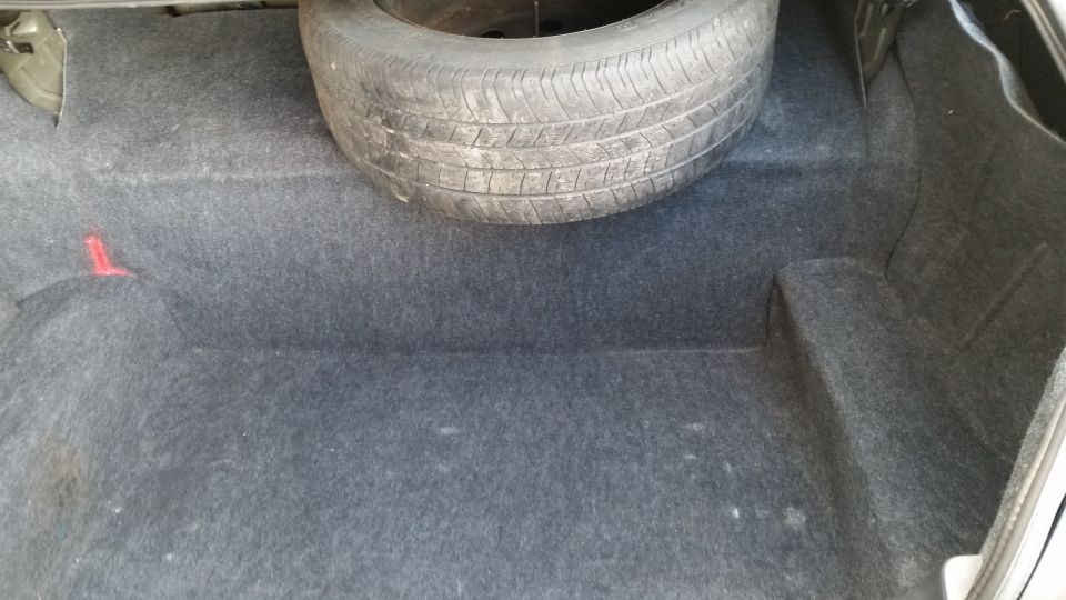 Car trunk interior showing grey carpet and a spare tire mounted on the right side