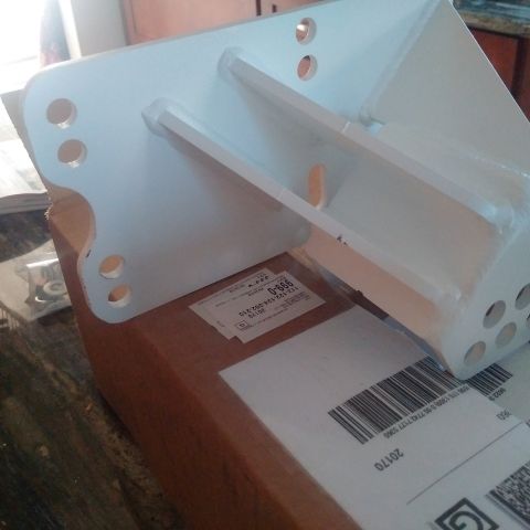 1978 Ford Bronco - White metal suspension part with bolt holes, placed on a cardboard box with shipping labels.