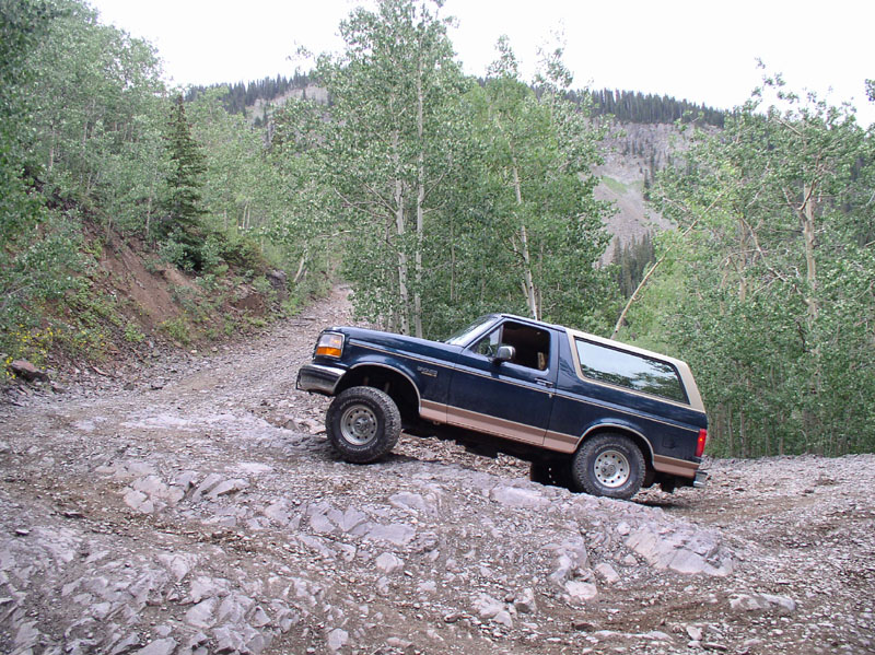 Dark blue and tan Ford Bronco climbing a rocky mountain trail through aspen trees