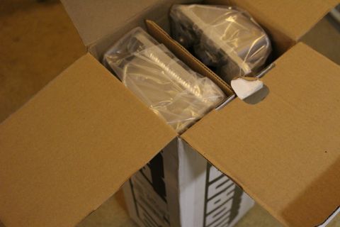 2003 Ford Crown Victoria - open cardboard shipping box revealing two plastic-wrapped metal parts packed inside.