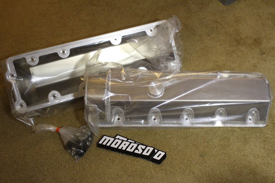 Two fabricated aluminum valve covers with hardware bag and a black Moroso badge on carpet