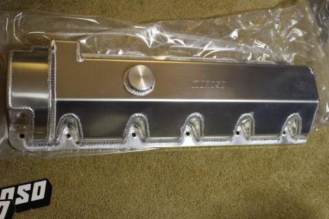 2003 Ford Crown Victoria - single fabricated aluminum valve cover with rope-welded bolt bosses and a round filler cap, resting in plastic wrap on carpet.