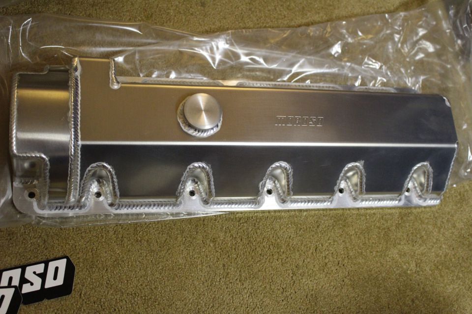 Single fabricated aluminum valve cover with welded bolt bosses and filler cap on carpet