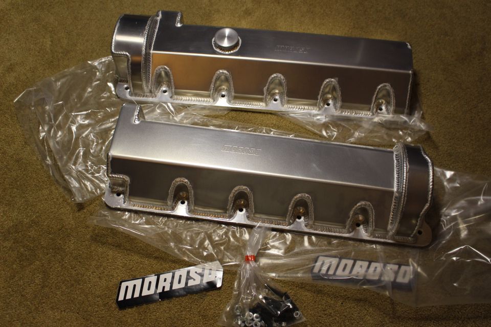 Two fabricated aluminum valve covers with filler cap, hardware, and MOROSO badges on carpet