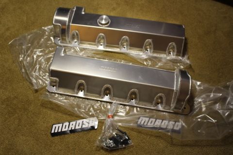 2003 Ford Crown Victoria - pair of brushed fabricated aluminum valve covers in plastic wrap with a hardware bag and two MOROSO badges on carpet.