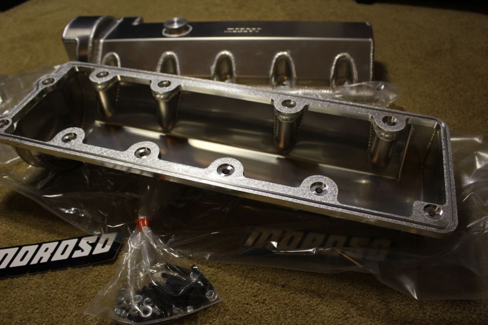 Underside of a fabricated aluminum valve cover with bolt holes, hardware bag, and MOROSO badges