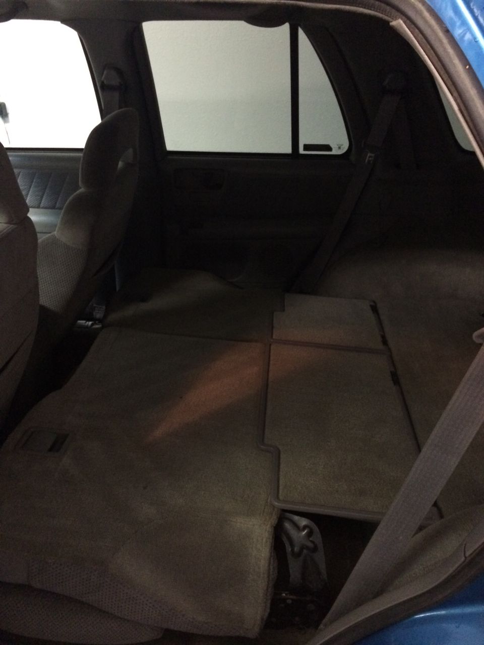Blue SUV interior, rear cargo area with folded seats. Seatbelts visible