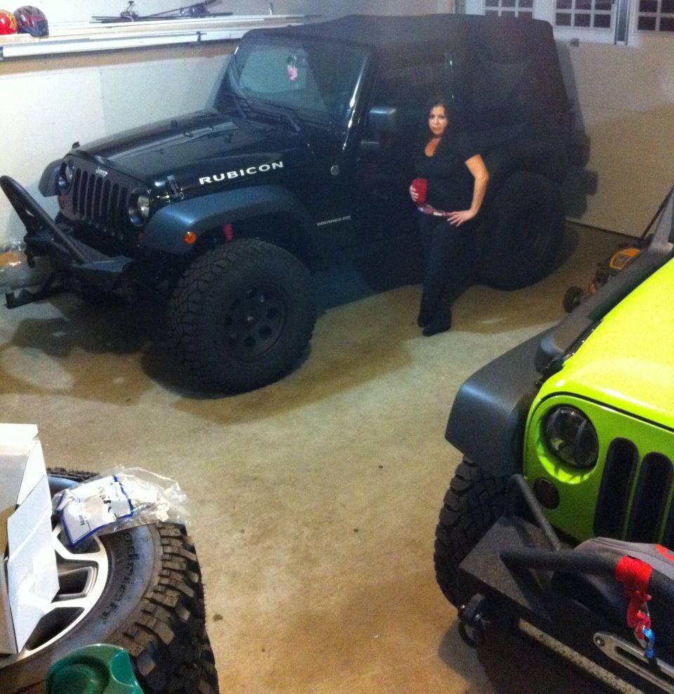 Black Jeep Wrangler with Rubicon badging and aftermarket bumper, parked indoors next to a lime green Jeep