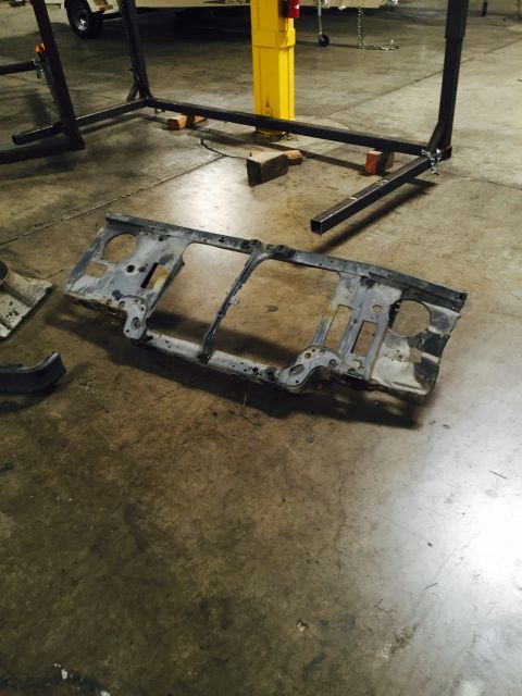 1988 Ford Bronco - A disassembled vehicle radiator support lies on a concrete floor, with a trailer and industrial equipment visible.