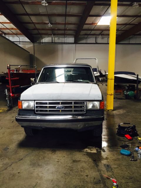1988 Ford Bronco - A white Ford Bronco is parked in a garage, showing its front end.