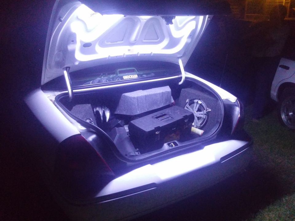 Trunk open with subwoofers and a toolbox inside. Another car is visible to the right