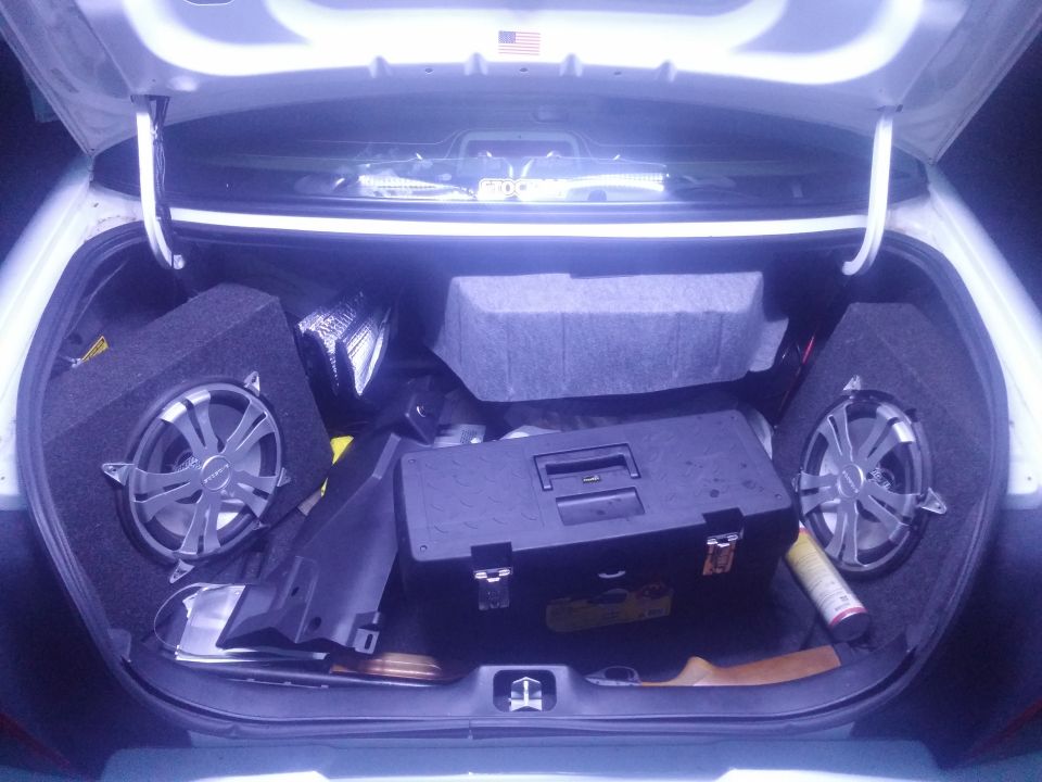 Trunk interior with two subwoofers, a black toolbox, and a can of spray paint