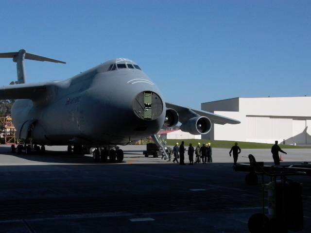 Gray C-5 Galaxy aircraft on tarmac, front view, with crew members nearby