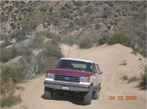 1990 Ford Bronco - This 1990 Ford Bronco navigates a dusty, off-road trail with arid hills in the background.