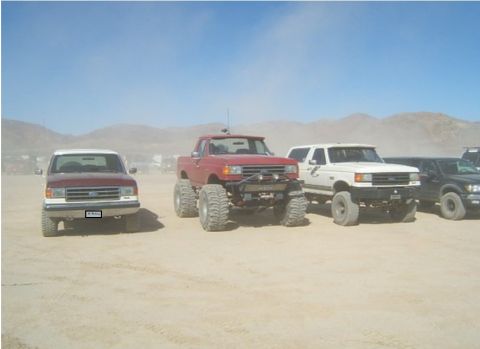 1990 Ford Bronco - Several off-road vehicles are lined up in a desert landscape under a clear blue sky.