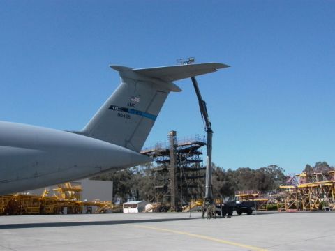 1990 Ford Bronco - A large military cargo airplane is parked on an airfield with a crane positioned near its wing.